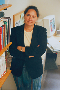 Dr. Jennifer. A. Giroux Giroux, a White female in a suit jacket standing next to bookshelf and computer.