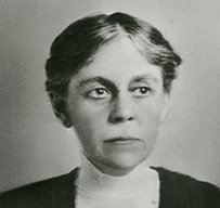 Dr. Alice Hamilton, a White female, in a jacket with her glasses hanging from a pocket, posing for her portrait.