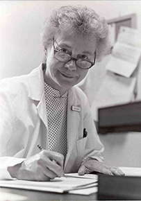 Dr. Réjane M. Harvey, a White female with glasses in a lab coat writing in a folder.
