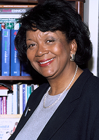 Dr. Renee Rosalind Jenkins, a smiling African American female posing in front of bookshelves.