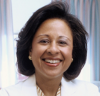 Dr. Paula A. Johnson, a smiling African American female in a lab coat standing in a patient's room.