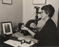 Dr. Irena Grasberg Koprowska, a White female  looking into a microscope at a desk.