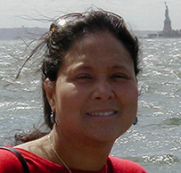 Dr. Elizabeth Theresa Lee-Rey, a smiling female with dark hair in a red blouse posing in front of the river and Statue of Liberty.