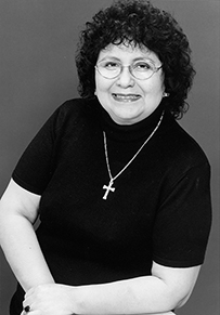 Dr. Delores Maria Leon, a White female with curly dark hair wearing a cross necklace posing for her portrait.