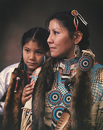 Dr. Sharon M. Malotte, an American Indian female in traditional Indian attire posing with a young girl with braids.