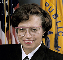 Dr. Audrey Elizabeth Evans, a White female in decorated military uniform and glasses posing in front of the American flag.