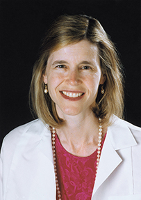 Dr. Joann Elisabeth Manson, a smiling White female wearing a lab coat and professional attire.