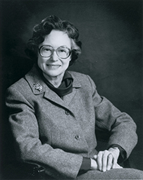Dr. Anne Bishop McKusick, a White female in a gray coat and glasses sitting on a chair, smiling for her portrait.