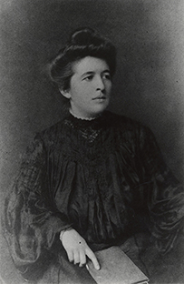 Dr. Dorothy Reed Mendenhall, a White female in a long sleeved gown seated with a book.