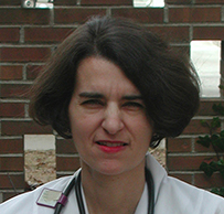 Dr. Flavia Elaine Mercado, a White female wearing a lab coat and stethoscope seated outdoors. 