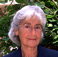 Dr. Doris Honig Merritt, an elderly White female in a blue suit seated in front of a green shrub.