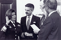 Dr. Antonia Novello, a White female in military uniform swearing in with one hand raised and one on a bible, in front of 4 people.