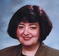 Dr. Adriana R. Padilla, a White female with dark short hair in a brown jacket posing for her portrait.