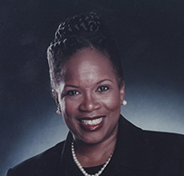 Dr. Lucille C. Norville Perez, a smiling African American female in a dark suit and pearls posing for her portrait.