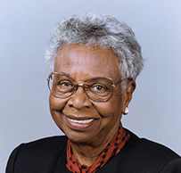 Dr. Muriel Petioni, a smiling African American female in a red scarf and dark jacket.