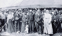 Dr. Susan La Flesche Picotte, the second from left, standing with a large gathering of people in front of a tent outdoors.