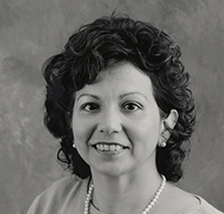 Dr. Teresa Ramos, a White female with short curly hair in pearls posing for her portrait.