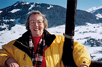 Dr. Edyth Hull Schoenrich, a White female in a yellow down coat, posing in front of a snow covered mountain top.