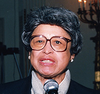 Dr. Jeanne Spurlock, an African American female wearing a name tag and scarf speaking into a microphone.