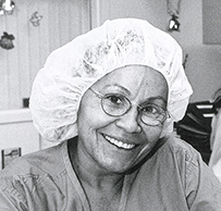 Dr. Victoria M. Stevens, an African American female in scrubs and a cap writing in a ledger while smiling for her photo.