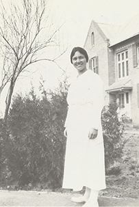 Dr. Lois Pendelton Todd, a female standing in a long dress in front of a home.