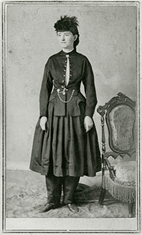 Dr. Mary Walker, a White female in a skirt, pants, and jacket standing next to a chair for her portrait.