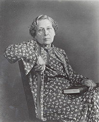Dr. Anna Wessels Williams, an elderly White female in a printed dress seated with a book in her lap for her portrait.