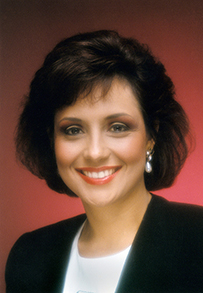 Dr. Michelle Anne Bholat, a smiling female with dark hair in a suit and a red background.