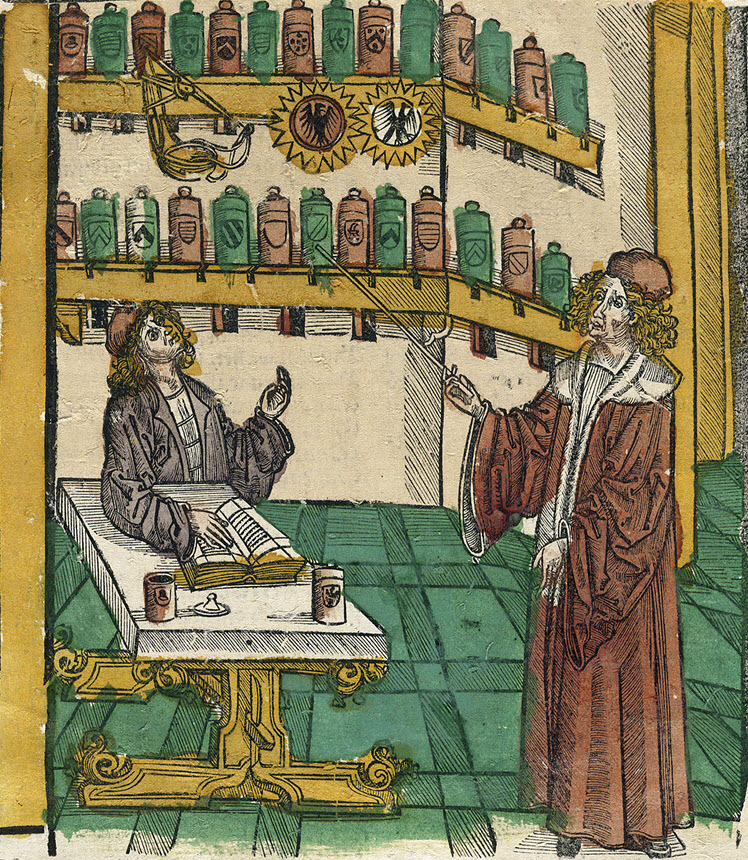 Man sitting with another man standing and gesturing with a wand. Bottles on shelves behind the men.