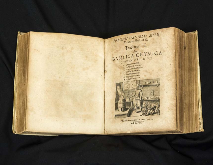 Open book showing printed text and image of an alchemy workshop.