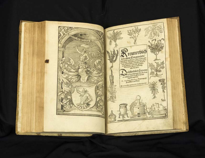 Open book showing printed text and illustrations of plants and distillation equipment.