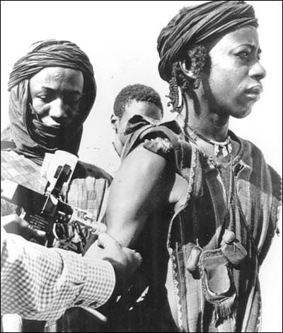 A person stands receiving a vaccination while two other people watch.