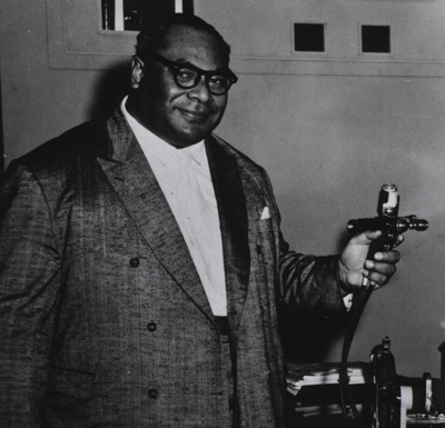 Three quarters, right pose of King Tauf-Ahau Tupou III of Tonga demonstrates a jet injector for smallpox immunization.