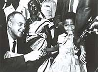 Surgeon General Stewart holds the hand of Rebecca Ansah Asamoah, a little girl who is biting her dress as she receives the 25 millionth smallpox inoculation.