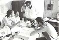 Smallpox Surveillance Unit sitting and standing around a table holding a discussion.