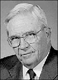 Head and shoulders, left pose of D.A. Henderson wearing glasses.