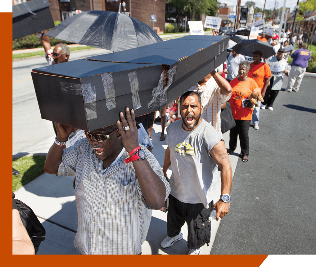 Two African American Men carrying a mock coffin. People process behind them.