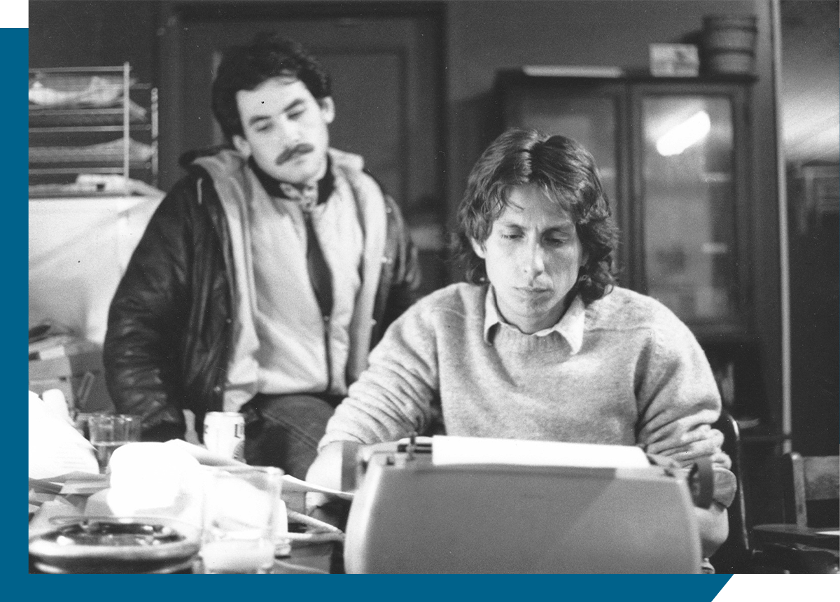 Callen on right seated in front of typewrite, Berkowitz on left leaning on desk.