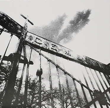 Fotografía en blanco y negro de unas rejas de hierro con el letrero “Cemetery” (“cementerio”) encima.