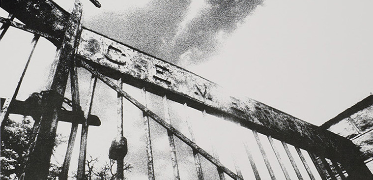 Fotografía en blanco y negro de unas rejas de hierro con el letrero “Cemetery” (“cementerio”) encima.