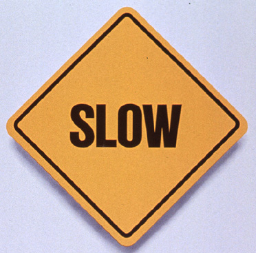 Yellow square road sign that reads “Slow” above text