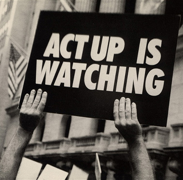 Black and white photograph of a pair of hands holding up a sign on a city street