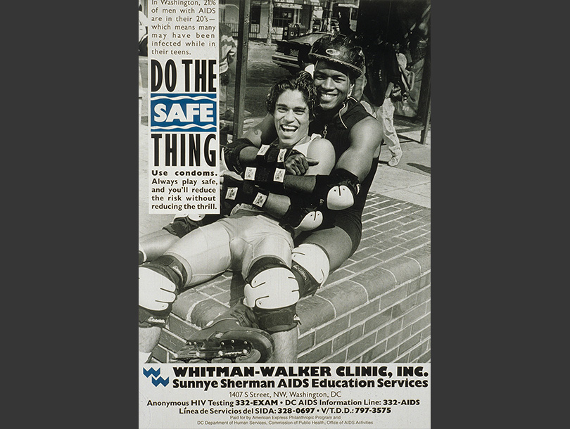 African American man sitting down and embracing a Latino man; both are wearing knee and elbow pads and one is wearing a helmet and rollerblades