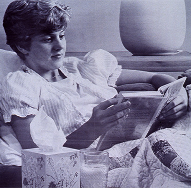 An advertisement showing text below a black and white photo of young white woman reading in bed, with tissues and a glass of liquid next to her
