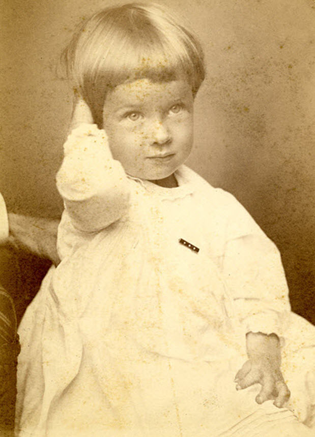 A young girl in dress, seated with right hand behind head, looks slightly to the right of viewer.