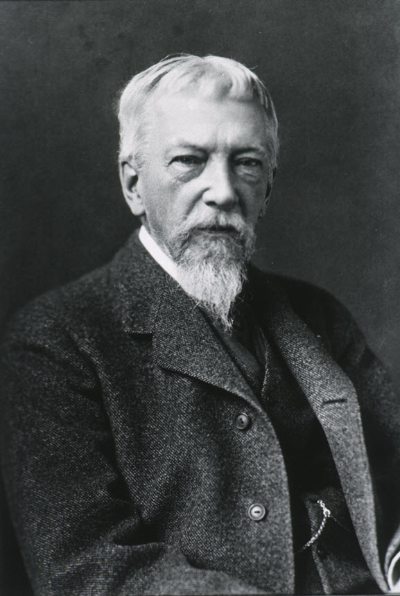 Elderly man with white hair and a beard, dressed in a suit looks slightly to the right of viewer.
