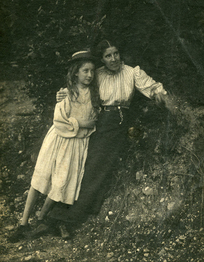 A woman and girl leaning against an embankment and looking off to the right .