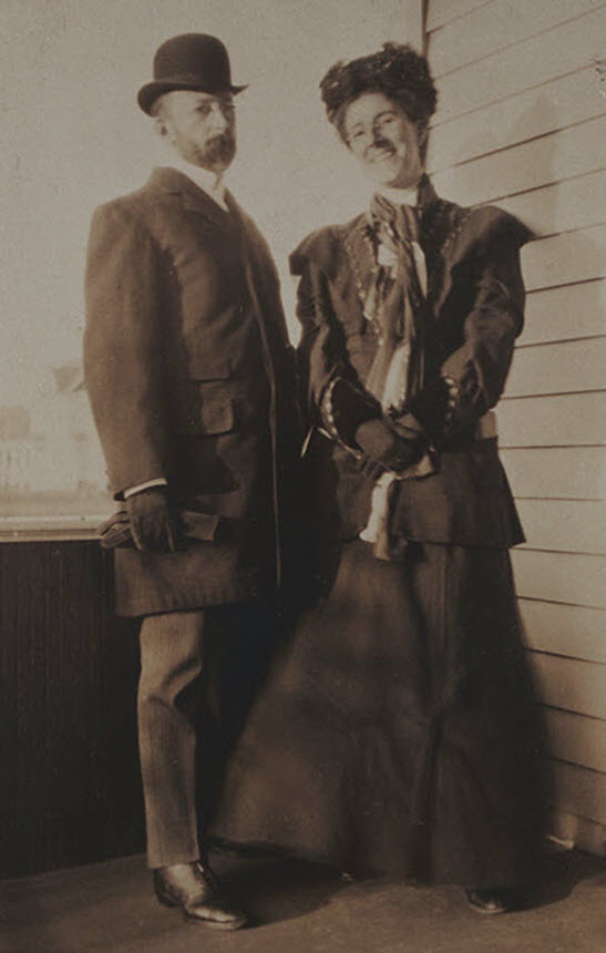 A woman and man standing on a porch in nice clothes, the woman is smiling.