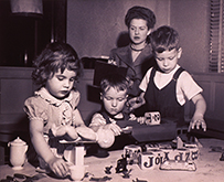 Three white children play with toys while a white woman looks on