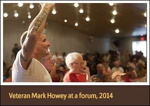 Man holds up arm with 'U.S. Army' tattooed on it, at a forum. 